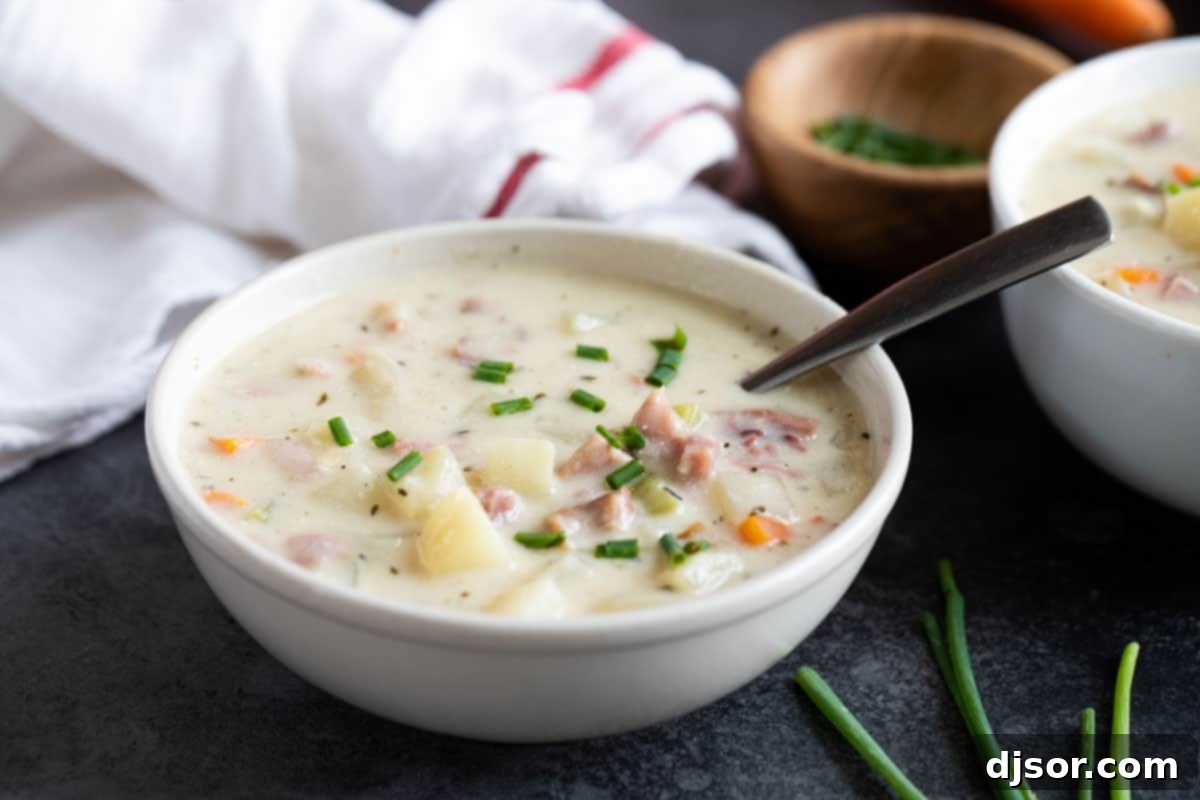 White bowl with ham and potato soup topped with fresh chives, ready to be served.