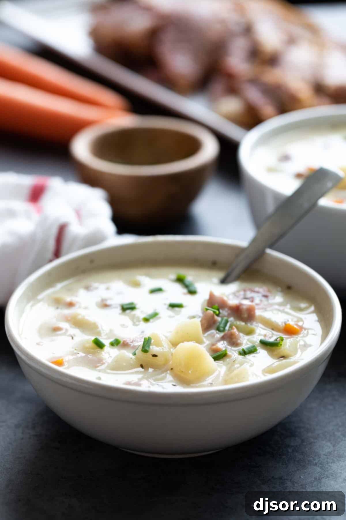 Close-up of a bowl of Ham and Potato Soup with a spoon, showing the creamy broth, tender potato chunks, and diced ham, garnished with fresh herbs.
