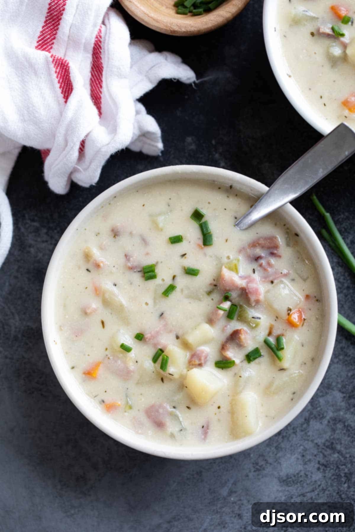 Another perspective of a white bowl of ham and potato soup, garnished with fresh chives, creating an inviting and appetizing presentation.