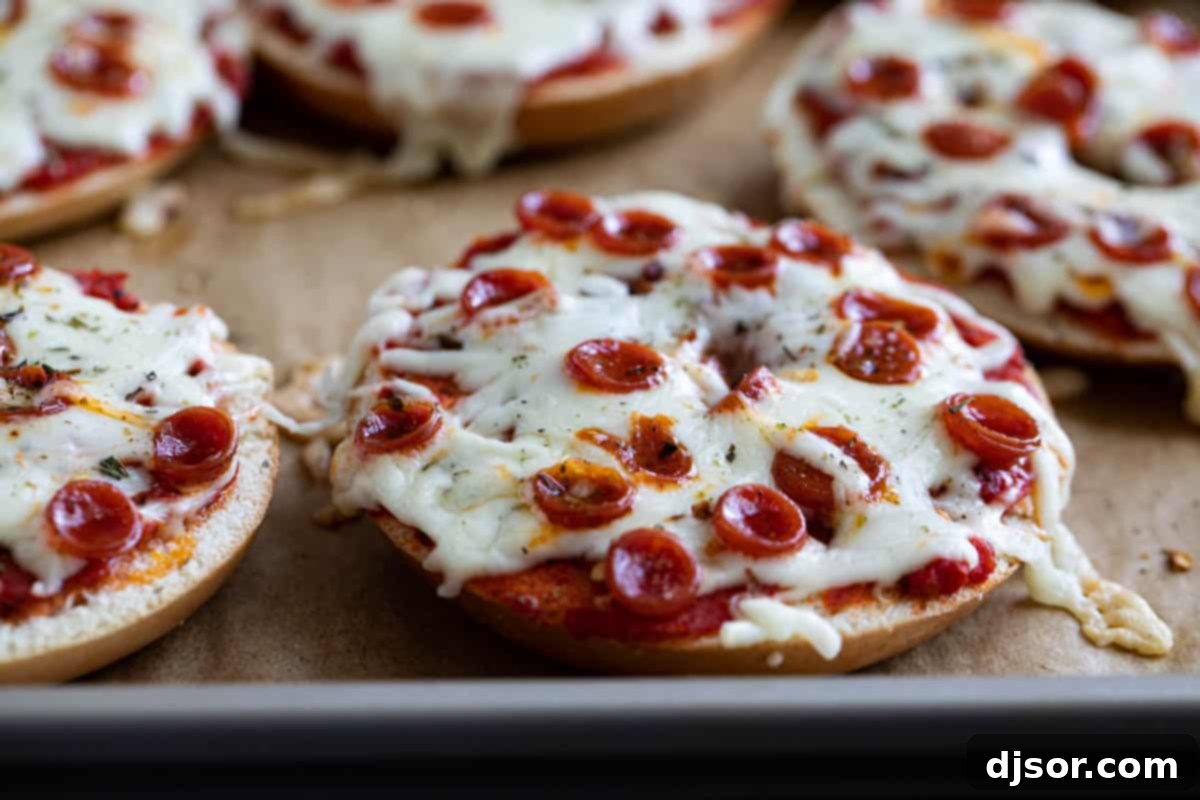 The Ultimate Bagel Pizza 2 Freshly baked pizza bagels topped with melted cheese and mini pepperoni, resting on a baking sheet.