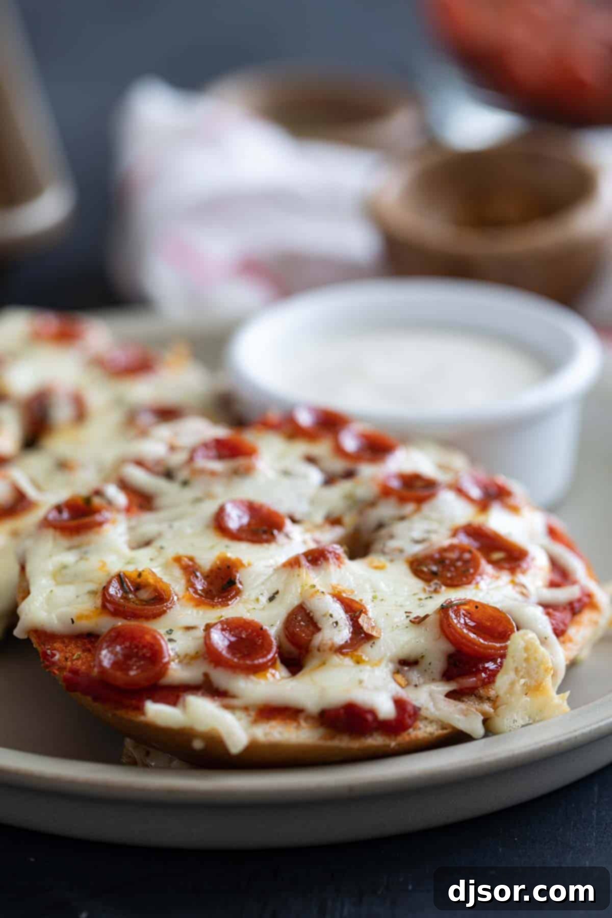 The Ultimate Bagel Pizza 6 A plate of pizza bagels served with a small container of ranch dressing for dipping, showcasing a perfect lunch or dinner.
