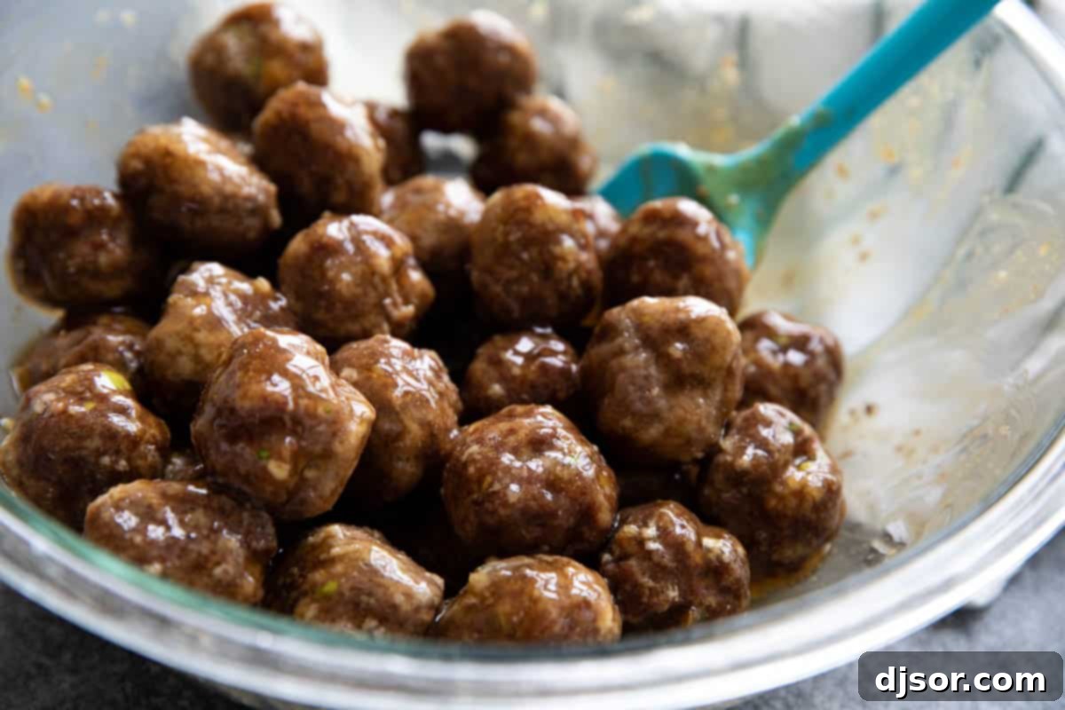These Teriyaki Meatballs are made with a delicious homemade teriyaki sauce that is super easy and fast. The meatballs are juicy and flavorful, and the sauce is sweet, tangy, and savory. This recipe is perfect for a quick and easy weeknight dinner, or for a party appetizer. Bowl with meatballs with teriyaki sauce stirred in.