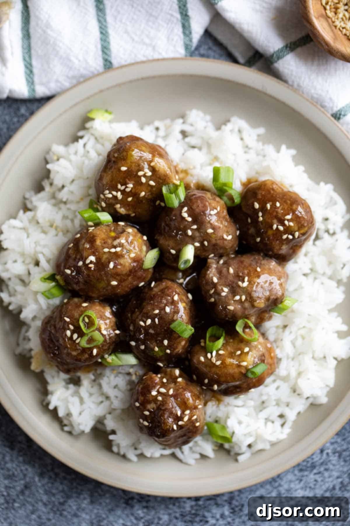 These Teriyaki Meatballs are made with a delicious homemade teriyaki sauce that is super easy and fast. The meatballs are juicy and flavorful, and the sauce is sweet, tangy, and savory. This recipe is perfect for a quick and easy weeknight dinner, or for a party appetizer. Plate with teriyaki meatballs on top of rice.