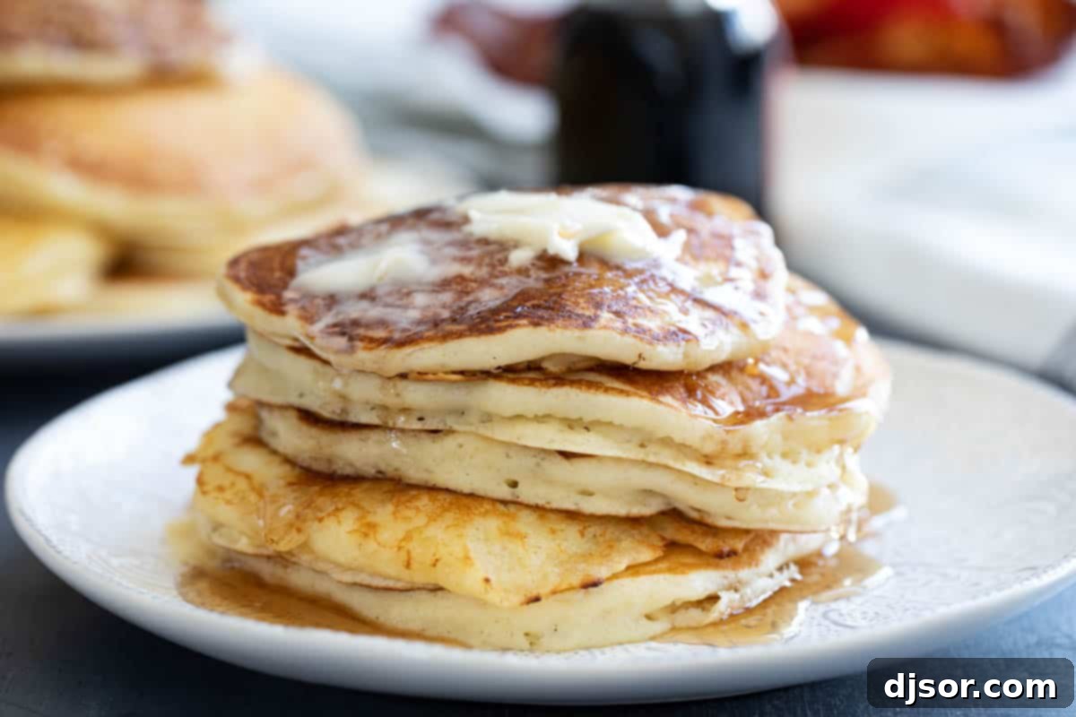 A tall stack of five golden-brown homemade buttermilk pancakes, drizzled generously with maple syrup and topped with a melting pat of butter, ready to be enjoyed.