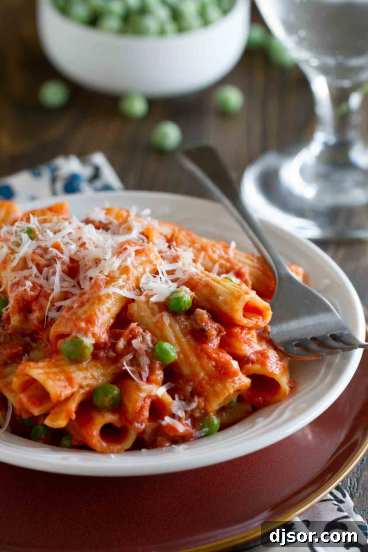A generously portioned dish of creamy rigatoni with Italian sausage, bright green peas, and a rich tomato sauce, ready to be served.