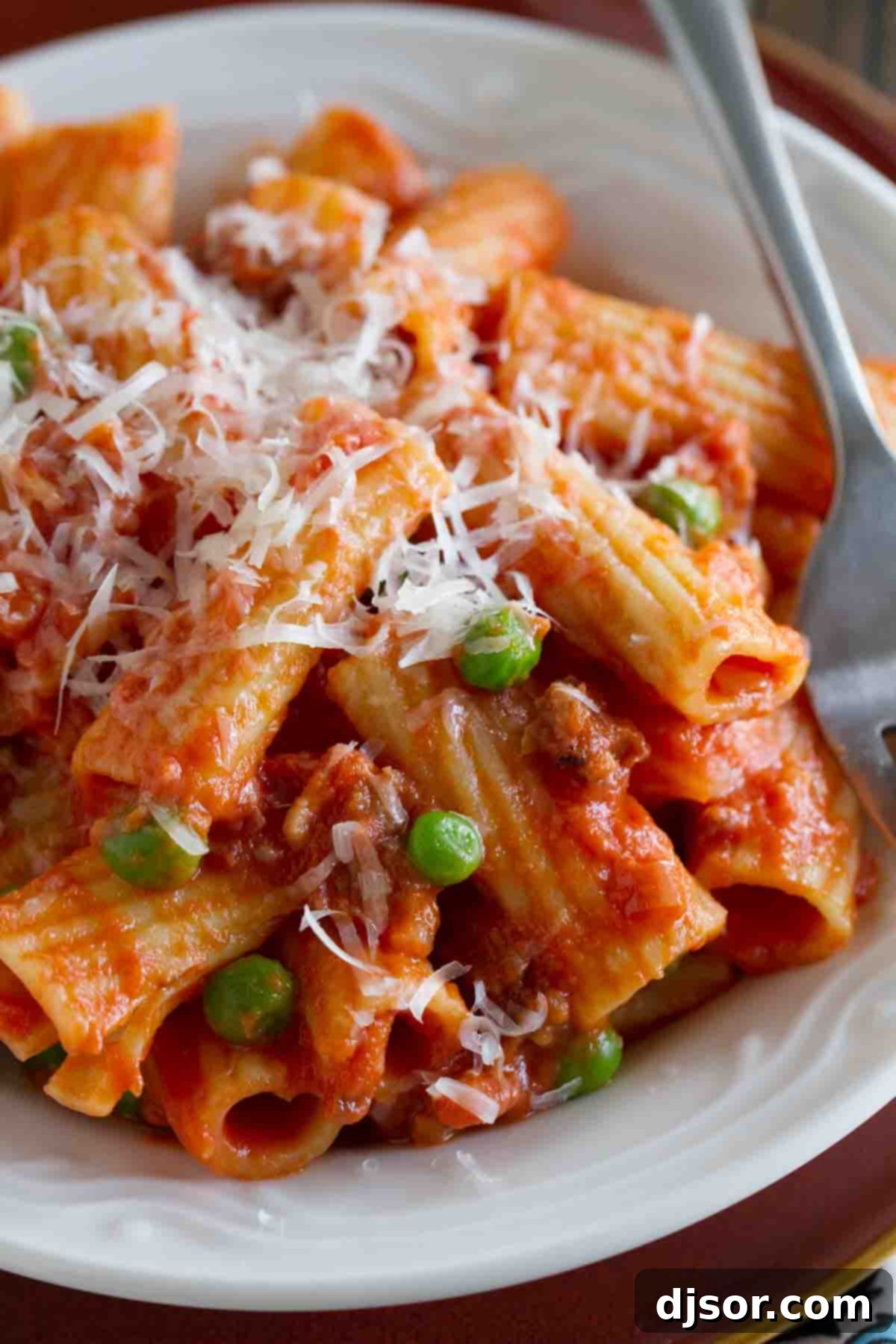 Close-up of creamy rigatoni with sausage, peas, and tomatoes, generously topped with freshly grated Parmesan cheese.
