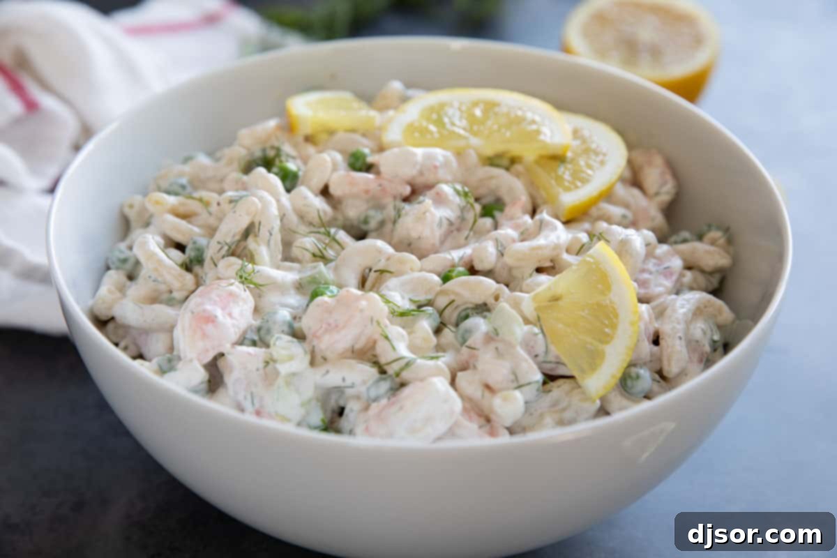 Bowl filled with shrimp pasta salad, topped with fresh dill and lemon slices.