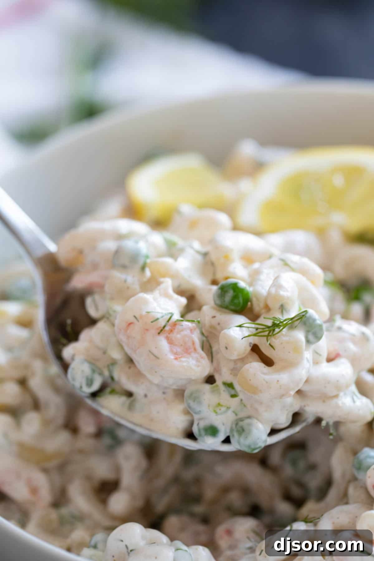 A serving spoon lifting a portion of shrimp pasta salad from a bowl.