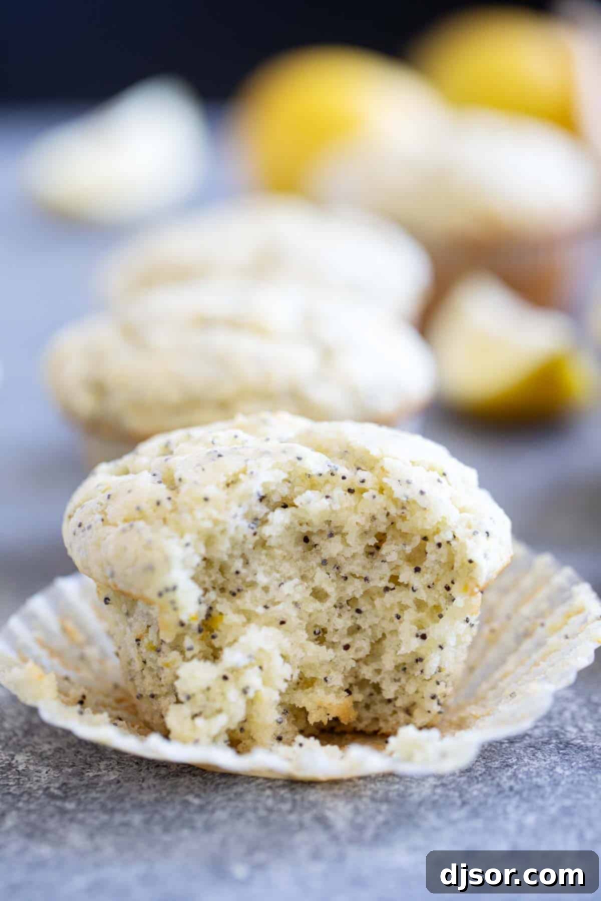 A close-up of a single Lemon Poppy Seed Muffin with a bite taken from it, revealing its moist, tender interior.