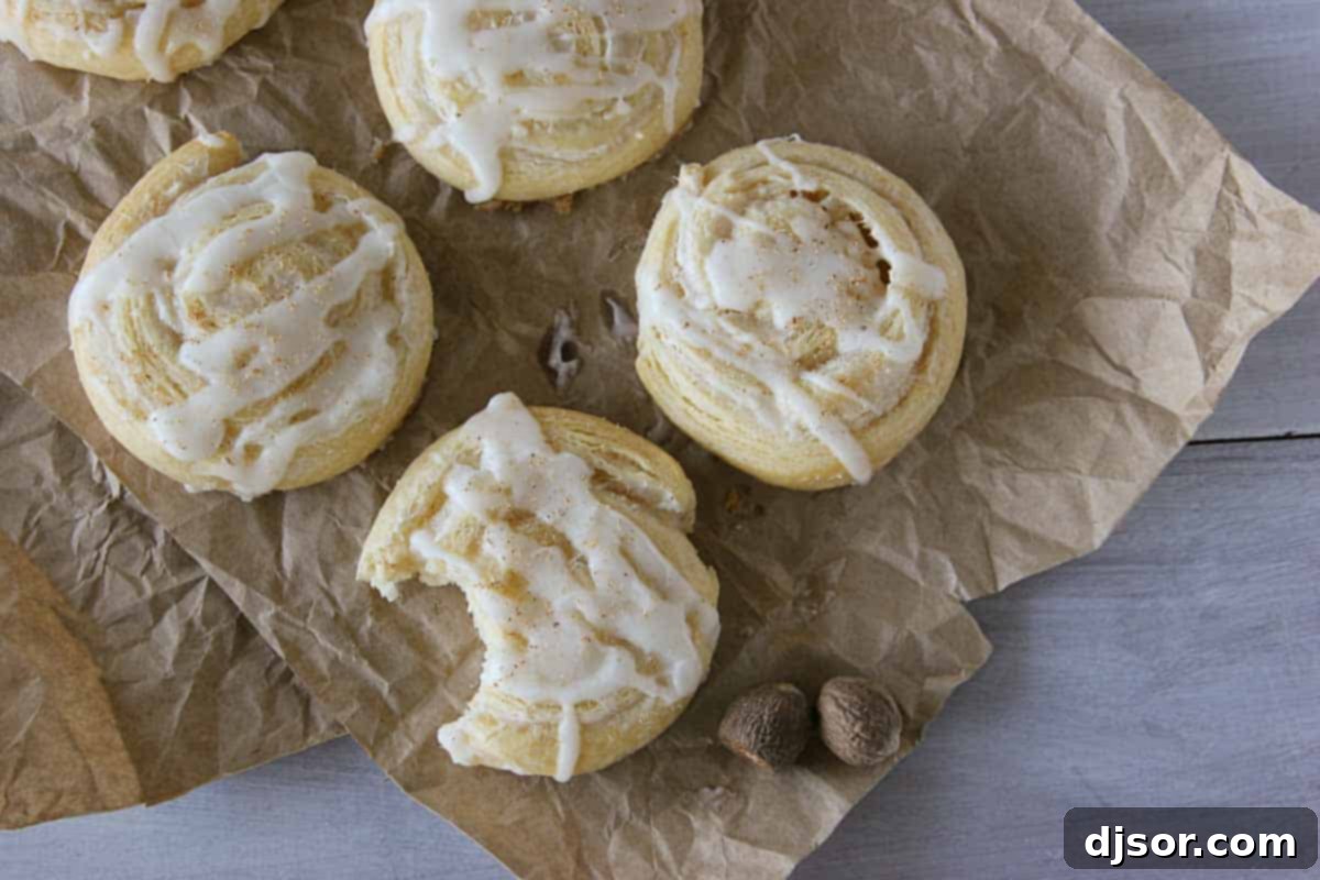 Spiced Eggnog Pinwheel Treats 4 Overhead view of Easy Eggnog Pinwheels on a rustic wooden surface, with one piece showing a bite taken out, revealing the soft, spiced cream cheese interior
