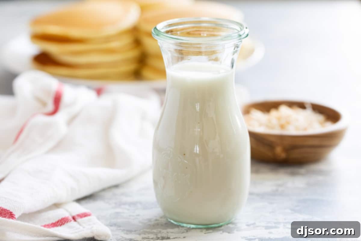 A clear glass container filled with freshly made, creamy coconut syrup, positioned with a stack of golden pancakes softly blurred in the background, ready for a tropical breakfast.