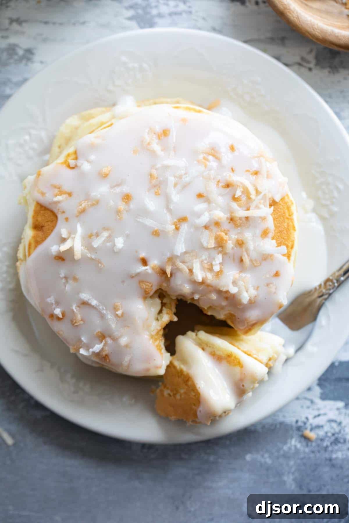 A tempting stack of golden pancakes, generously drizzled with homemade coconut syrup and adorned with toasted coconut flakes, with a fork digging into a fluffy bite, showcasing the perfect breakfast indulgence.
