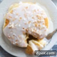 Stack of pancakes topped with coconut syrup and toasted coconut with a fork full of pancakes.