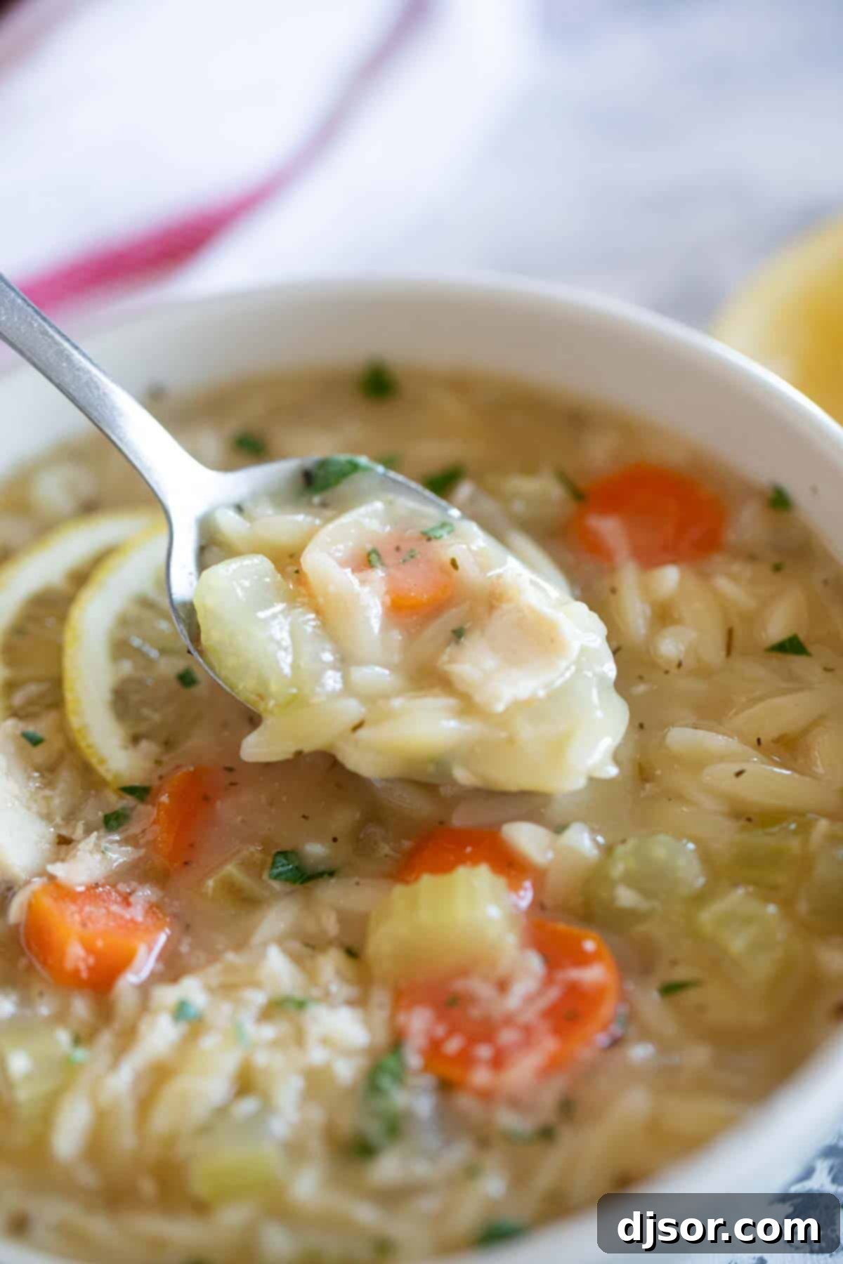 A spoonful of delicious Lemon Chicken Orzo Soup ready to be enjoyed. A close-up shot of a bowl of Lemon Chicken Orzo Soup with a spoon lifting a scoop, highlighting the rich broth and ingredients.