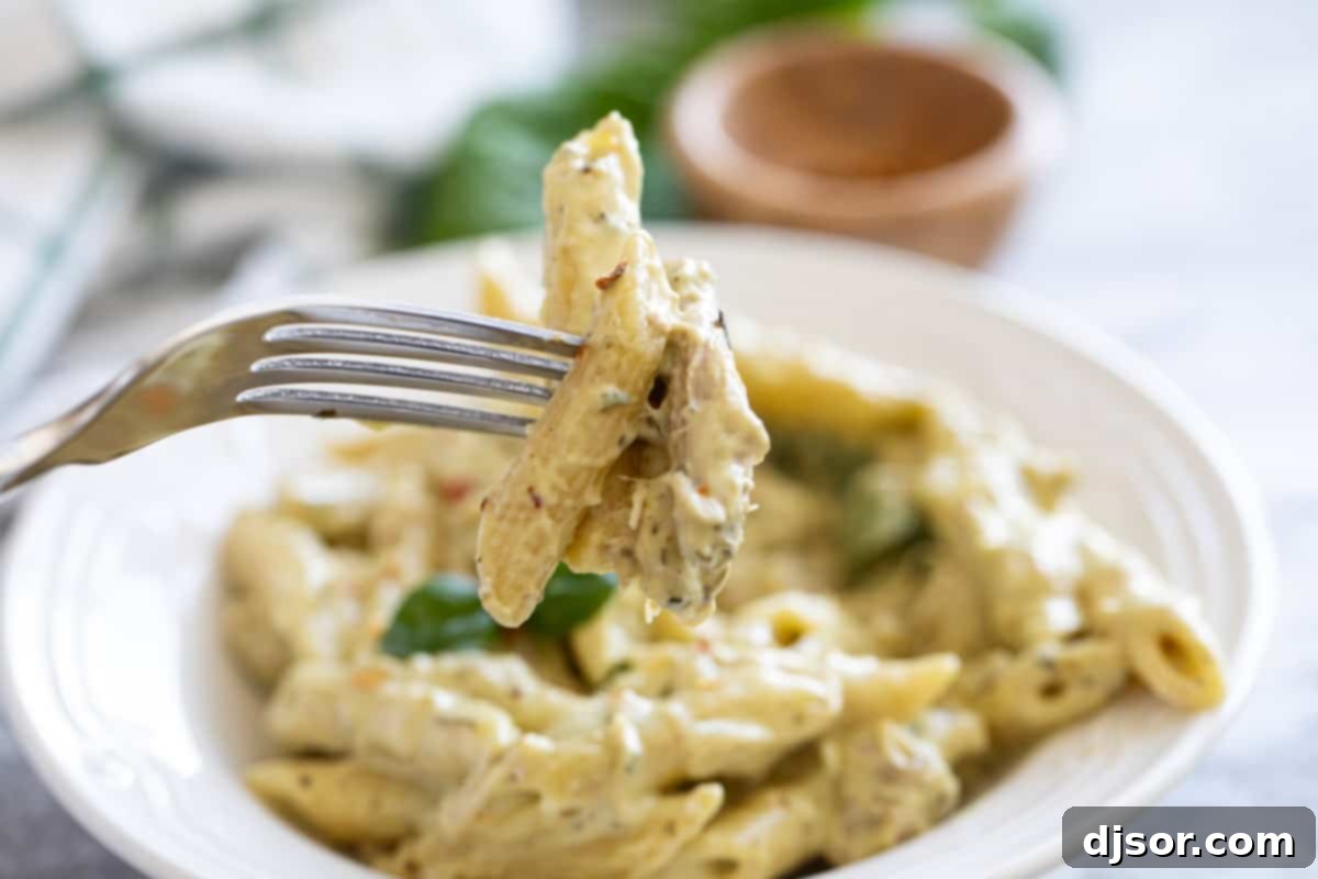 Creamy Pesto Chicken Pasta 7 Fork with pasta and chicken with a bowl of the pasta behind.