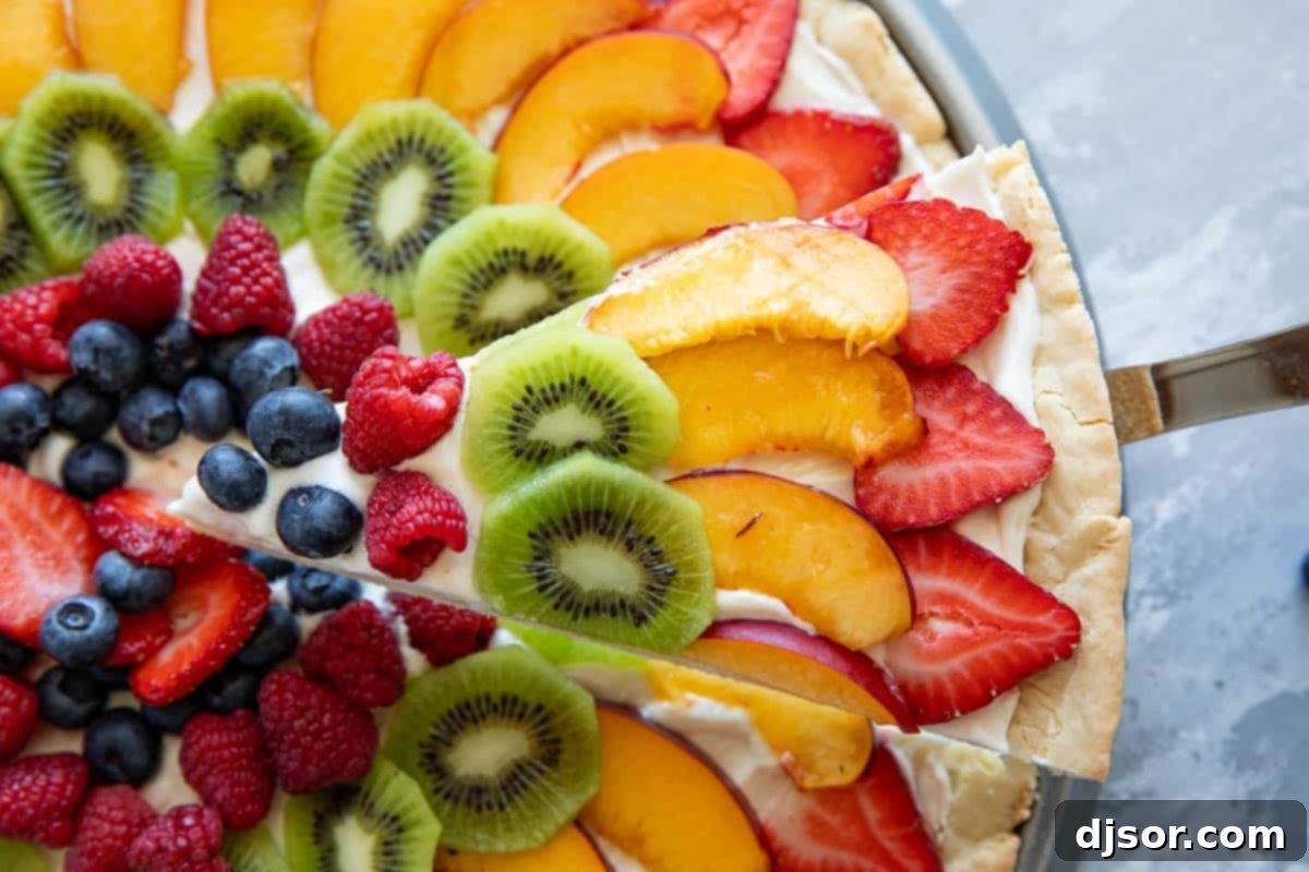 Indulge in the sweetness of summer with this irresistible Fruit Pizza. A sugar cookie base is topped with a sweet cream cheese frosting, then layered with fresh, in season fruit for a stunning dessert that is as delicious as it beautiful. Slice of fruit pizza topped with strawberries, peaches, kiwi, and berries.