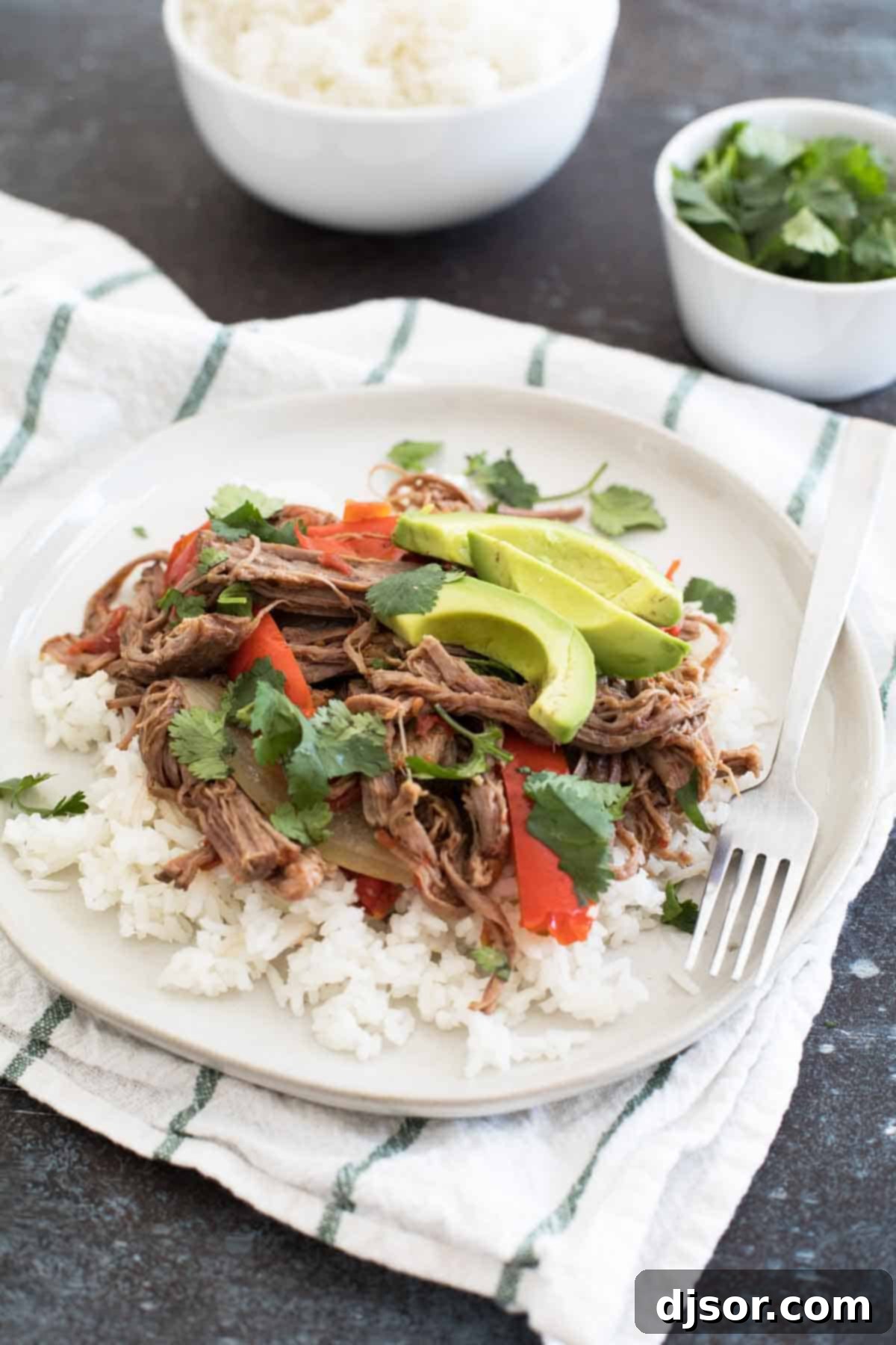 Fall-Apart Slow Cooker Cuban Ropa Vieja 3 Close-up of shredded slow cooker beef Ropa Vieja served over fluffy white rice, topped with creamy avocado slices and vibrant cilantro.