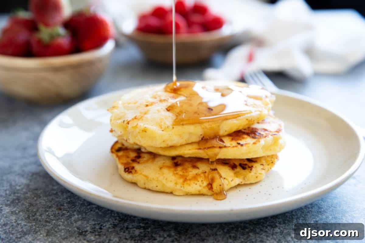 Three cottage cheese pancakes stacked on a plate with syrup being poured over them.