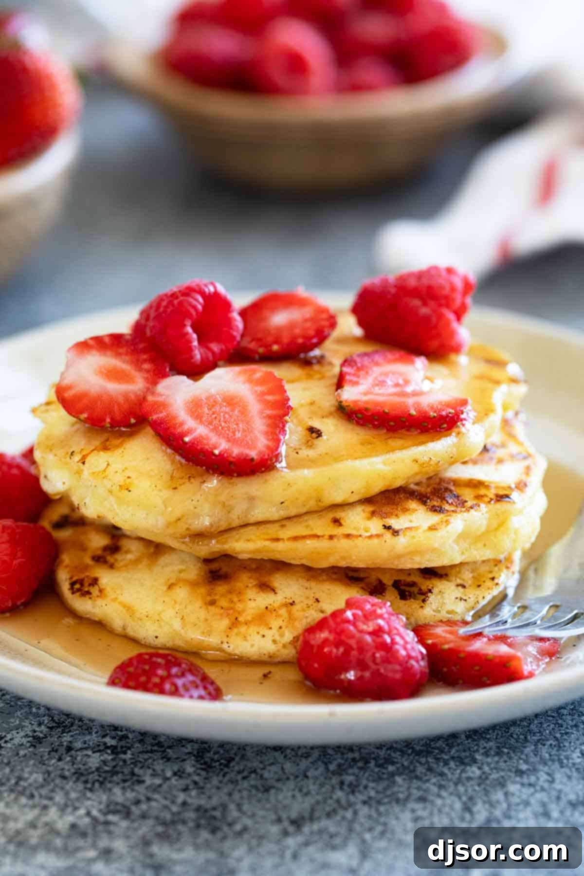 A stack of golden-brown cottage cheese pancakes topped with a generous drizzle of syrup and fresh mixed berries.