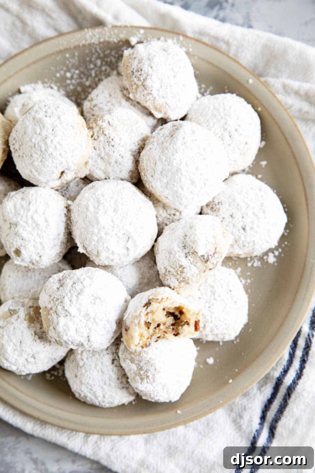 Mexican wedding cookies stacked on a plate, with a bite taken from one cookie.