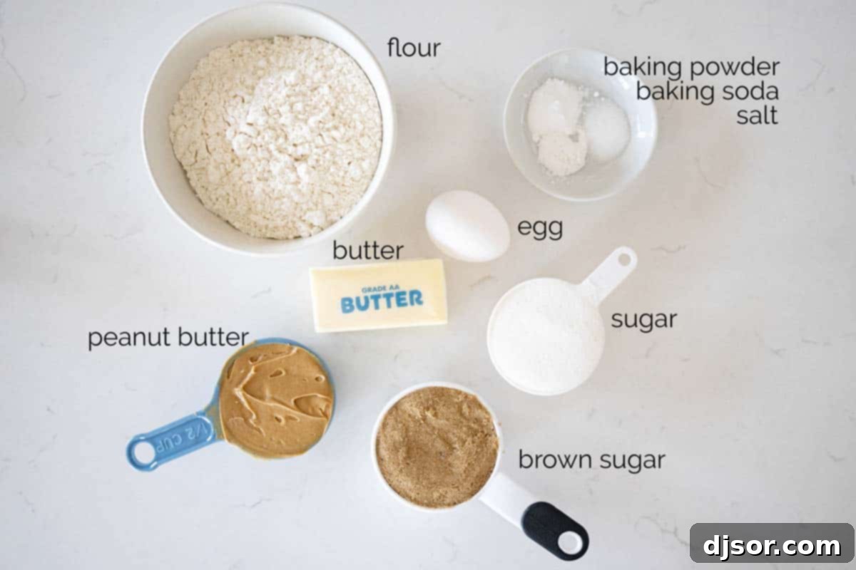 Fresh ingredients laid out on a table, including peanut butter, butter, sugars, an egg, flour, baking soda, baking powder, and salt, ready for baking classic peanut butter cookies.