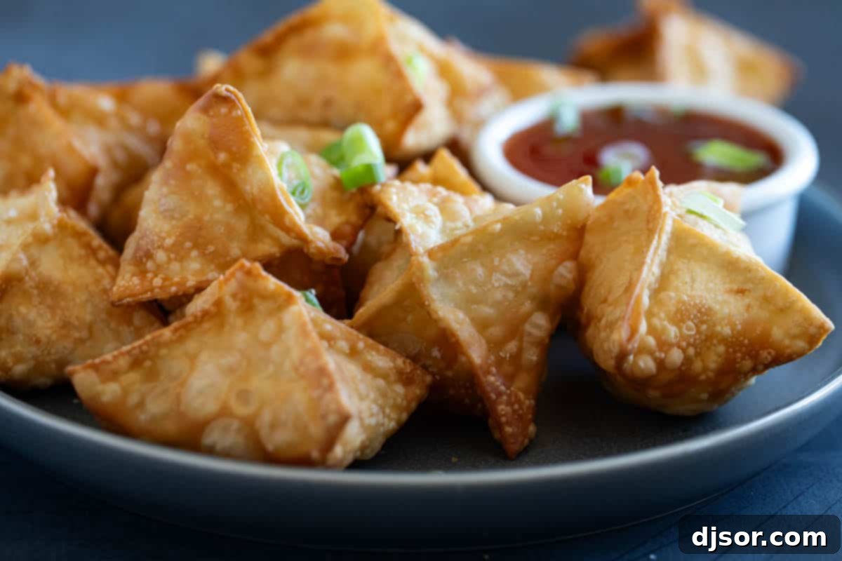 Plate with fried crab rangoon, with bowl of sweet chili sauce for serving.