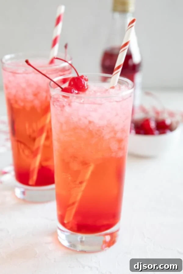 Two elegantly presented glasses filled with the vibrant Shirley Temple mocktail, each topped with a bright maraschino cherry.