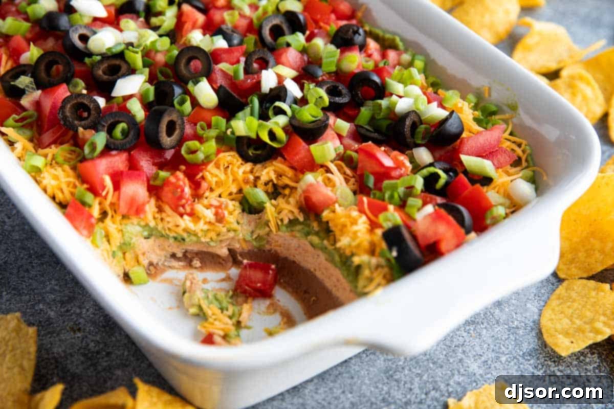 Dish with 7 layer dip, with some of the dip taken from the corner.