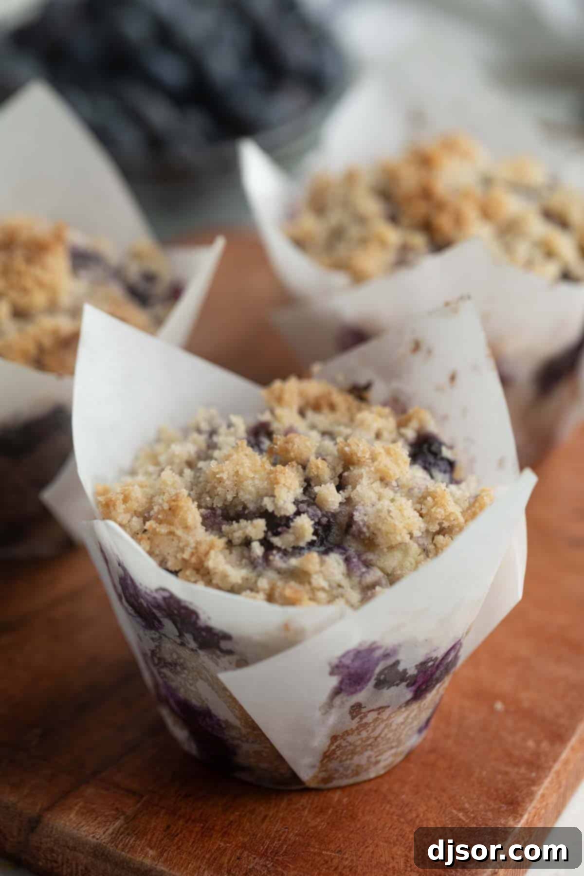 Freshly baked blueberry muffins with a golden crumb topping on a rustic wooden board.
