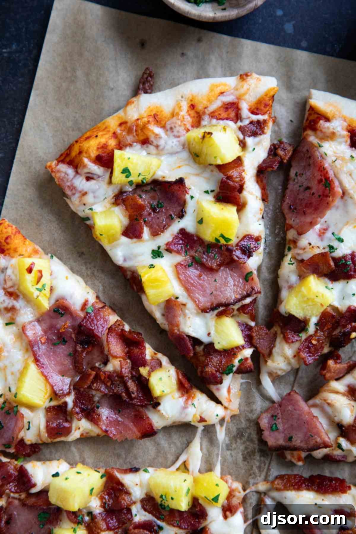 A close-up of a single slice of Hawaiian pizza, showcasing a perfectly golden crust, rich melted cheese, and generous pieces of ham, crispy bacon, and sweet pineapple.