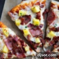 Slice of Hawaiian pizza topped with ham, bacon, and pineapple.
