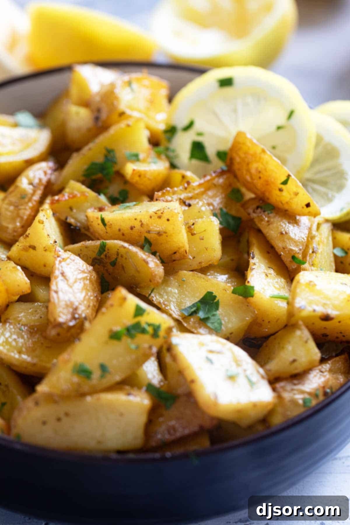 Zesty Greek Lemon Potatoes 7 Bowl filled with roasted Greek Lemon Potatoes sprinkled with fresh parsley and lemon wedges.