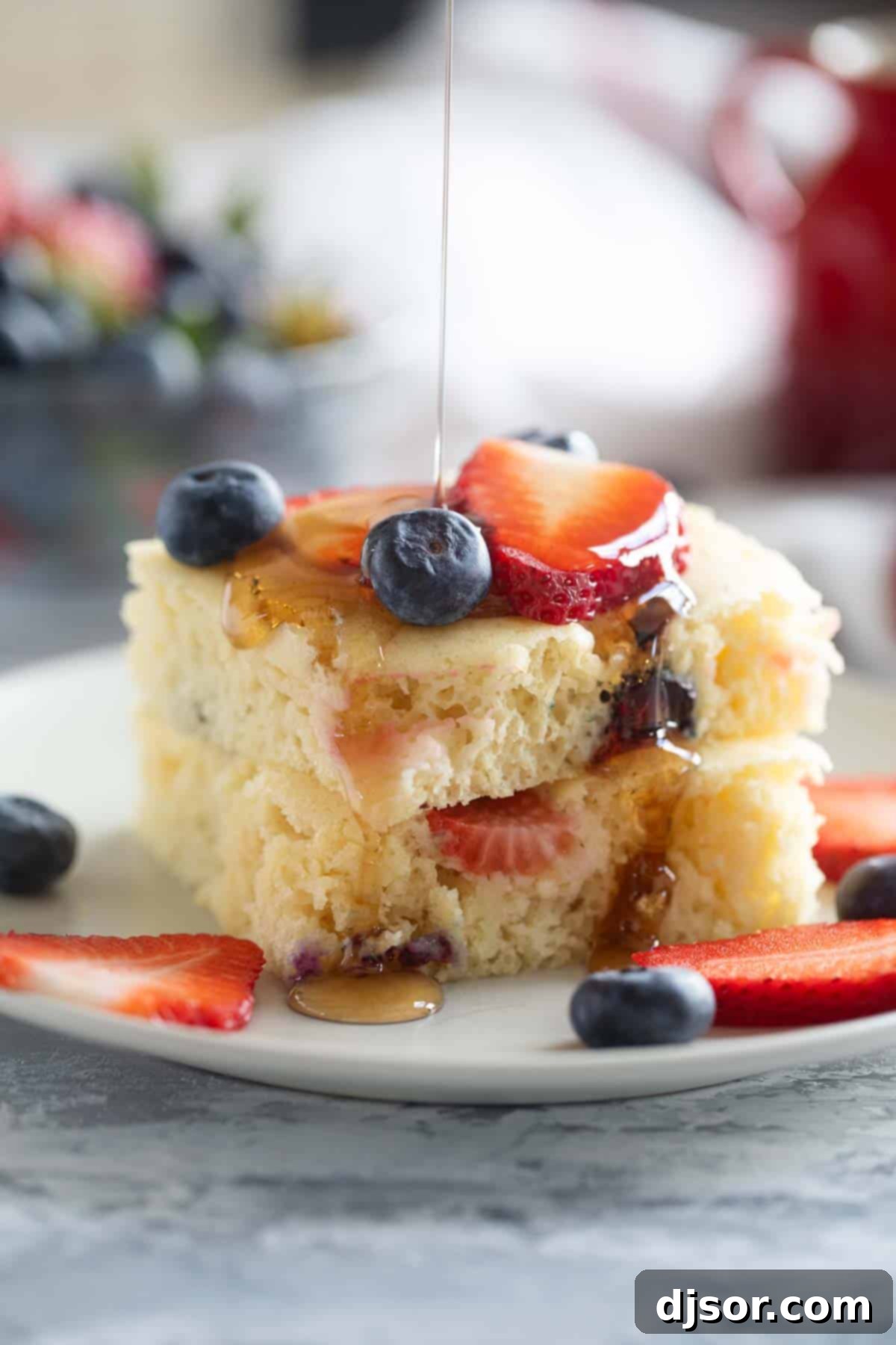 Sheet pan pancakes stacked on a plate with syrup being drizzled over the top.