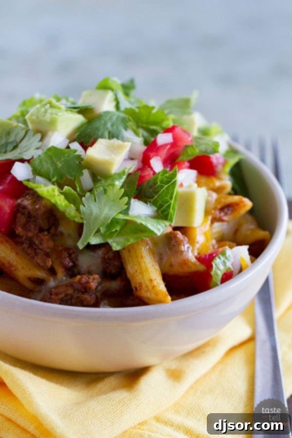 A vibrant, close-up shot of Taco Pasta Toss in a large serving bowl, featuring penne pasta, seasoned ground beef, melted cheese, fresh tomatoes, lettuce, avocado, and cilantro, ready to be served. Ideal for family dinners and Taco Tuesday.