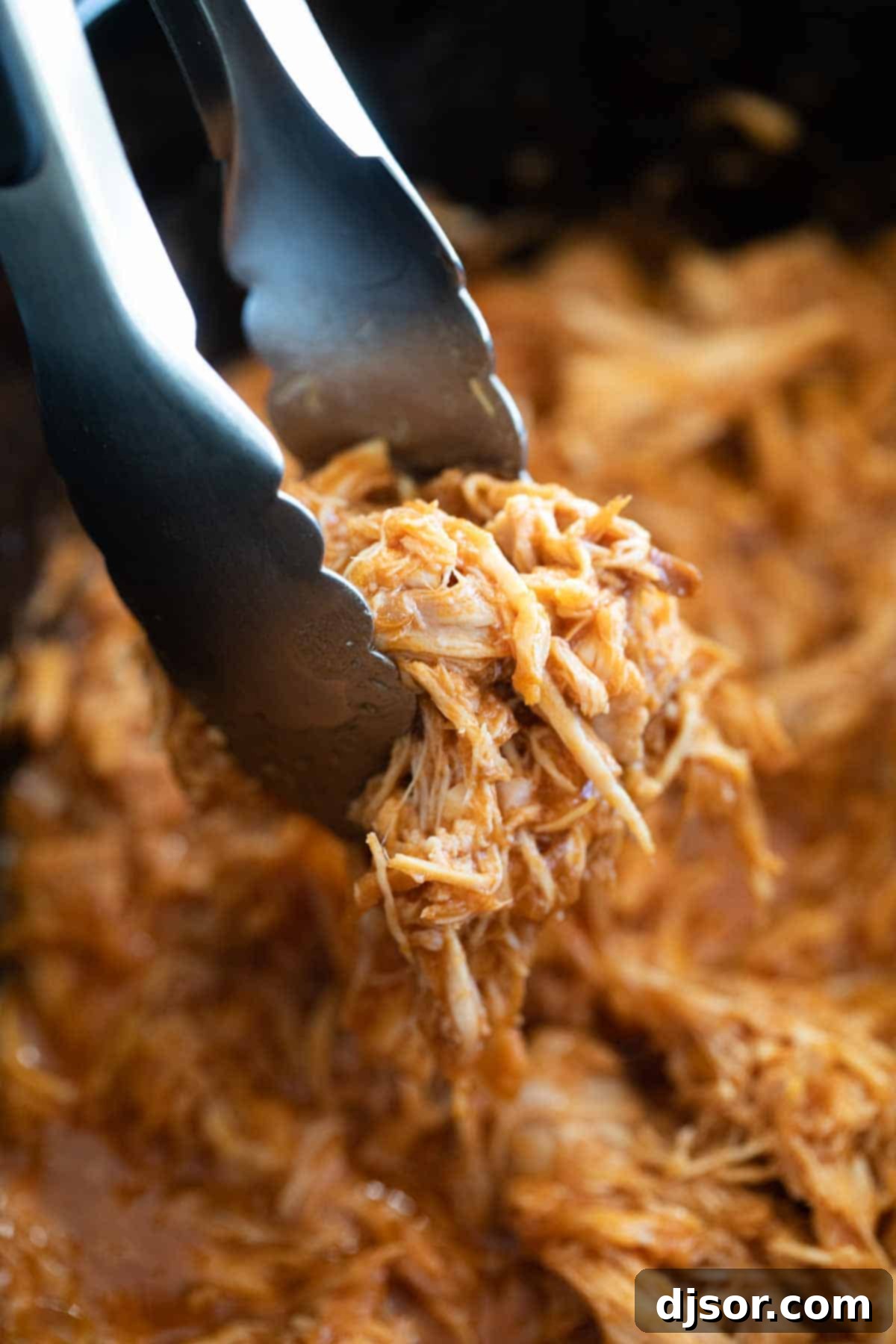 Slow Cooker Pulled Chicken Ready for Shredding Tender slow cooker pulled chicken being lifted with tongs.