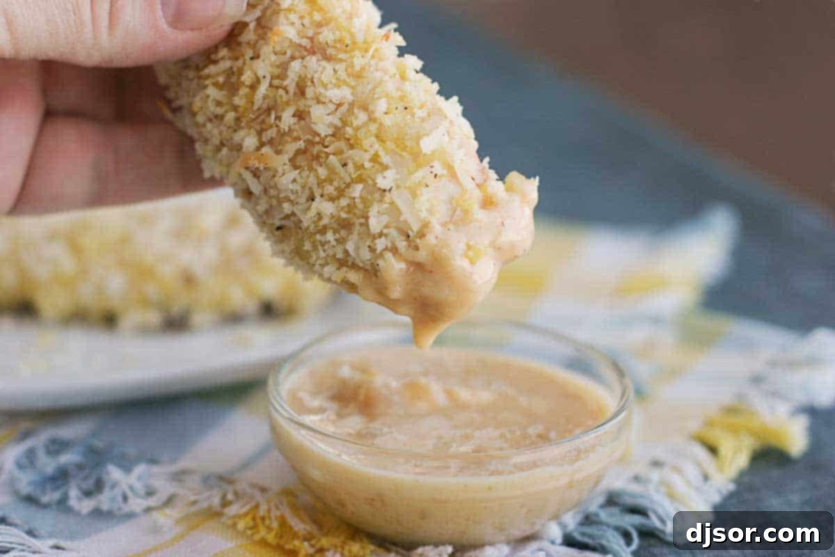 A close-up shot of a Coconut Chicken Tender being dipped into a bowl of creamy mango chutney, highlighting the crisp texture and rich dip.