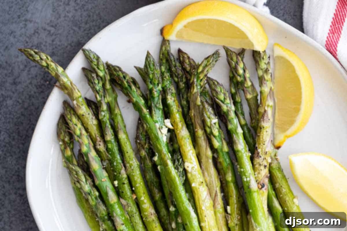 A serving of perfectly roasted asparagus spears on a white plate, garnished with fresh lemon slices, highlighting its vibrant green color and slight caramelization.