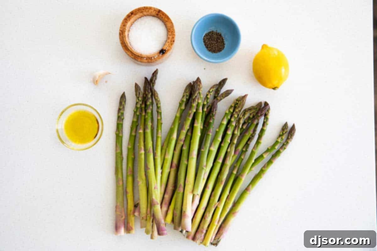 A flat lay image displaying the fresh ingredients required for roasted asparagus: a bundle of green asparagus, a head of garlic, a lemon, a bottle of olive oil, and salt and pepper shakers.