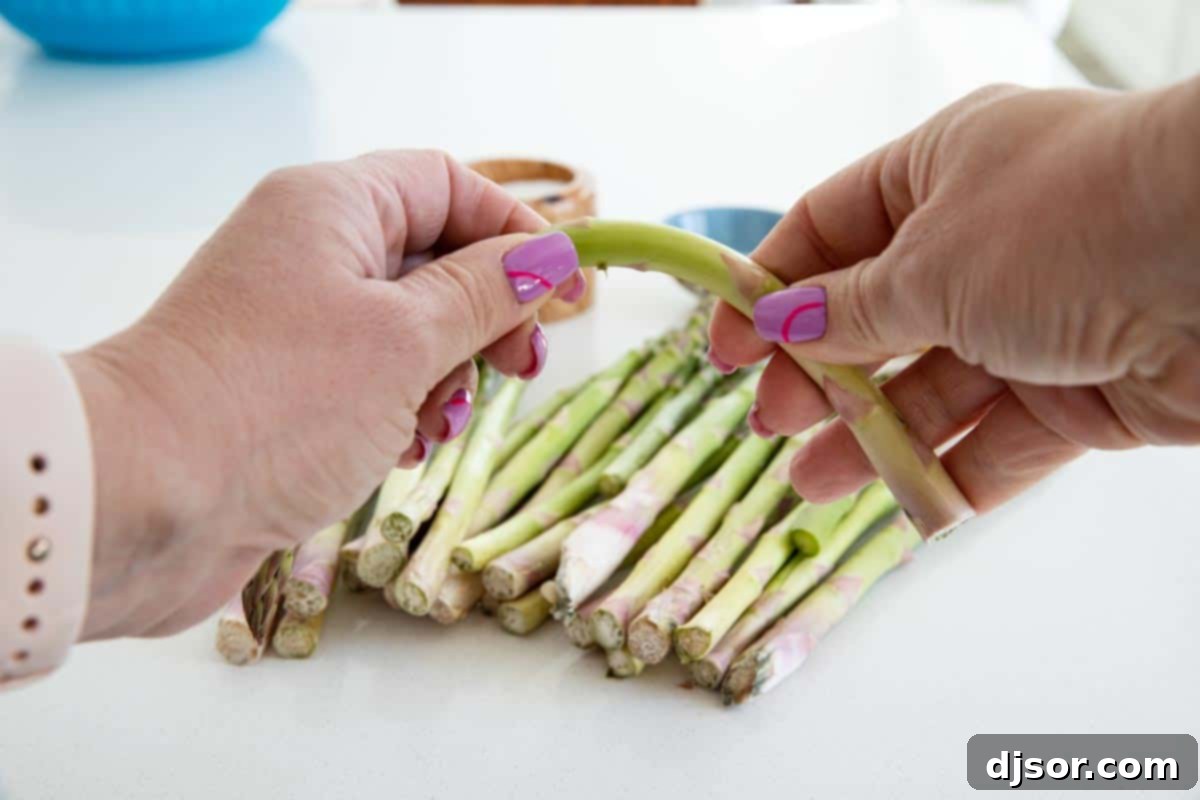 Close-up of a hand demonstrating the 'bend and snap' method to trim the woody end off a single asparagus stalk.