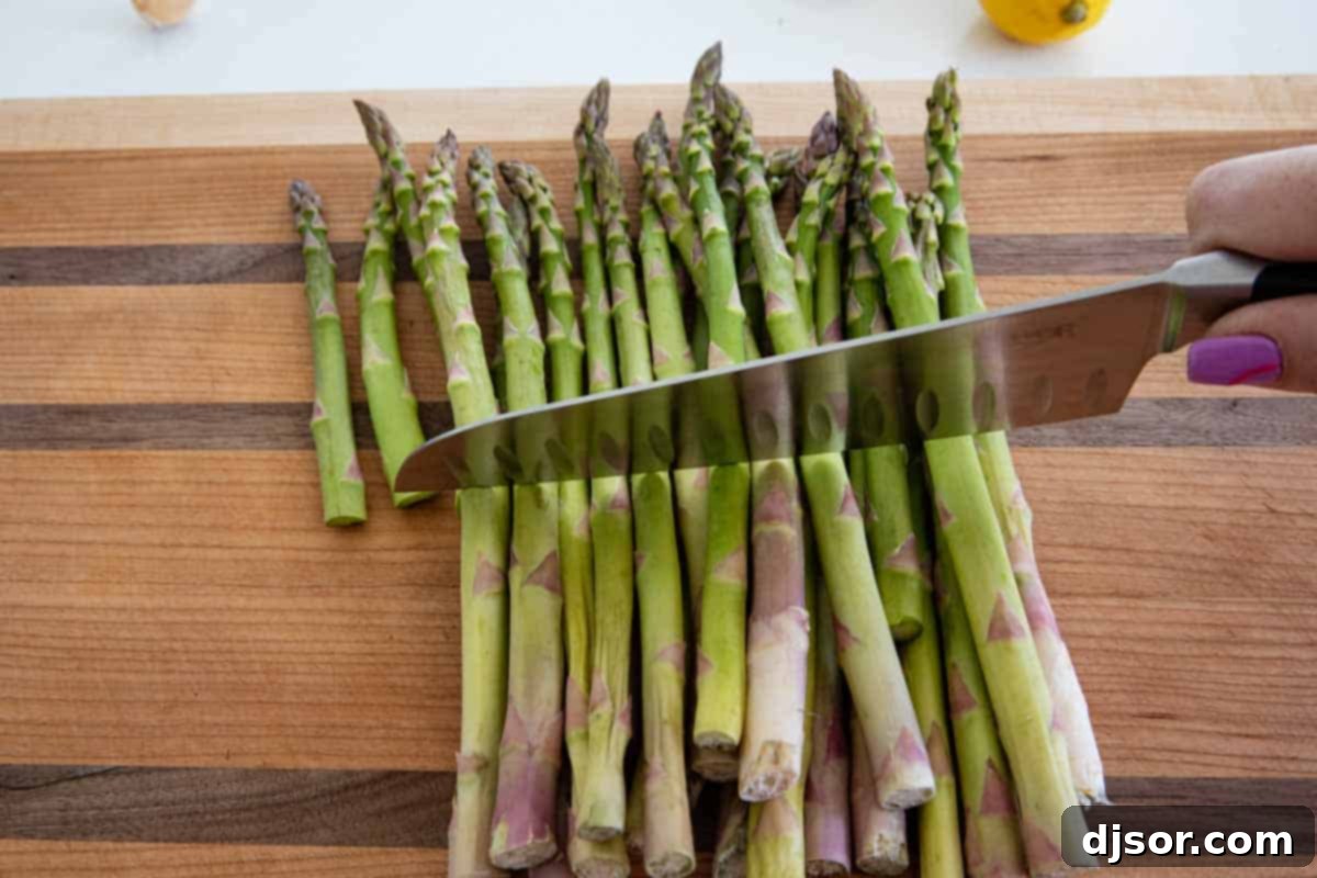 A cutting board with a bundle of trimmed asparagus and a knife, showing the uniform cuts made based on a guide stalk, with the woody ends discarded.