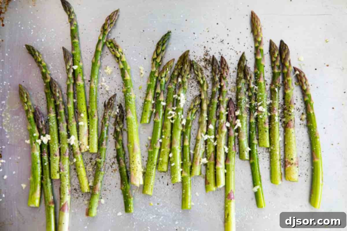Untrimmed asparagus spears laid out on a baking sheet, ready to be seasoned with olive oil and minced garlic.