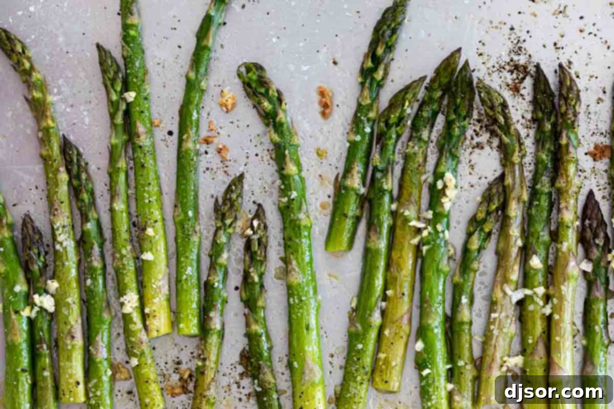Roasted asparagus spears, golden brown and tender, on a baking sheet, glistening with olive oil and hints of garlic.