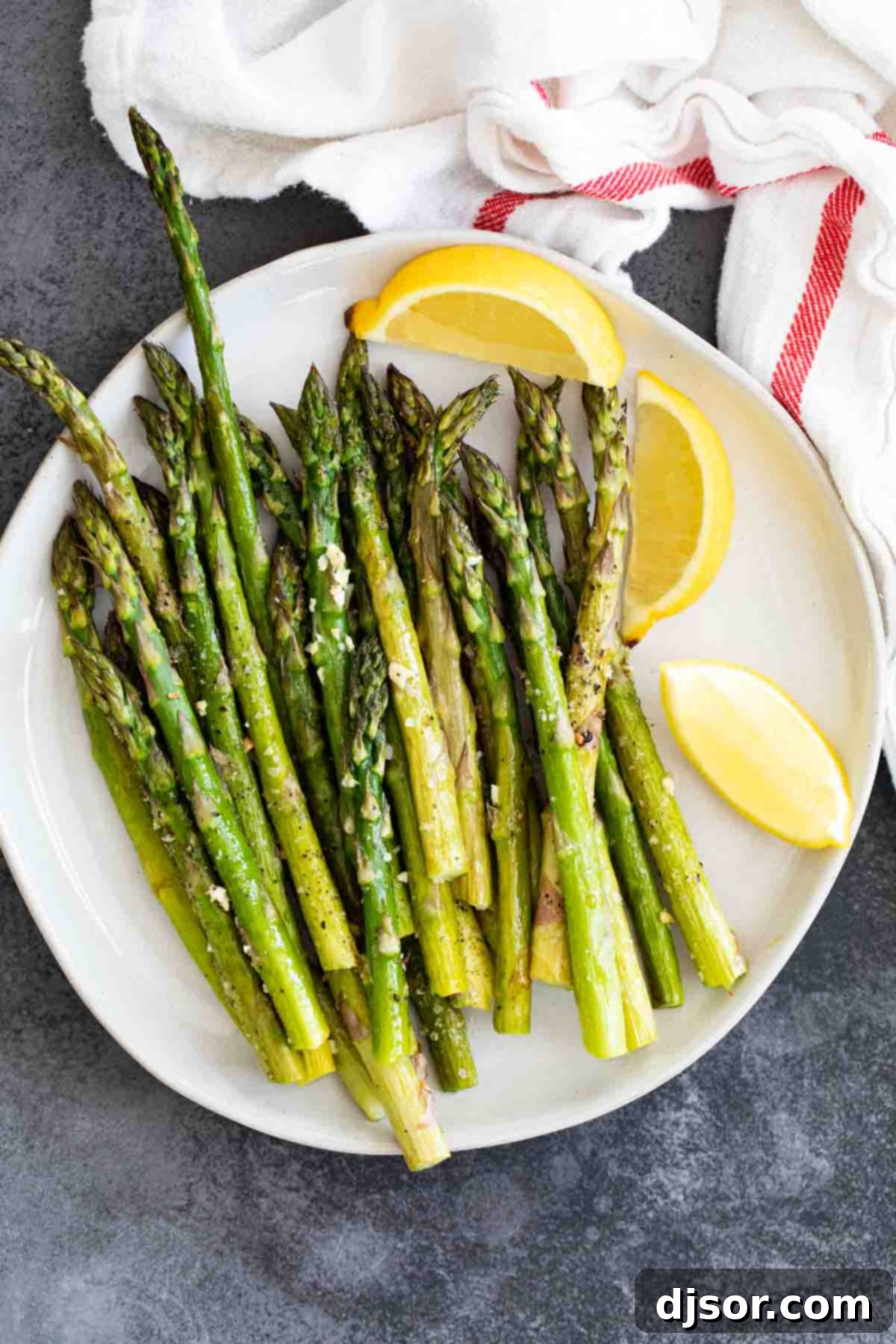 An overhead view of a white plate filled with beautifully roasted asparagus, garnished with fresh lemon wedges, ready to be served as a healthy side.