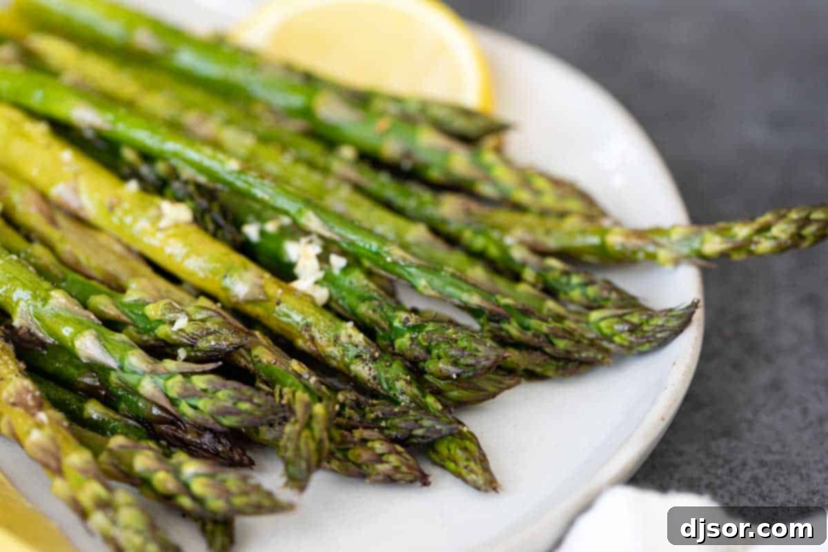 A close-up of tender, golden-brown roasted asparagus on a white plate, garnished with a single lemon slice, ready to be enjoyed as a vibrant side dish.