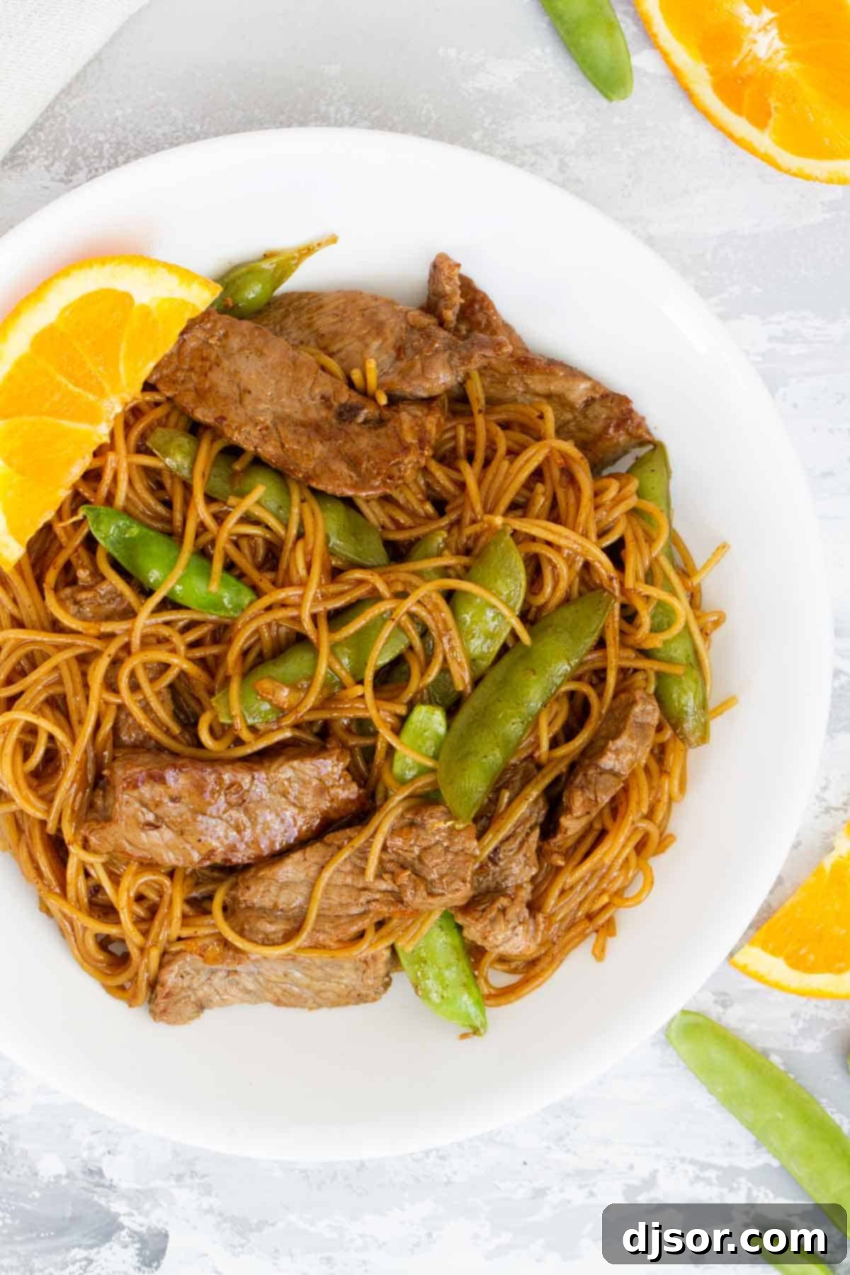 Vibrant Orange Teriyaki Beef with Noodles served on a white plate, garnished with fresh orange slices and green onions.