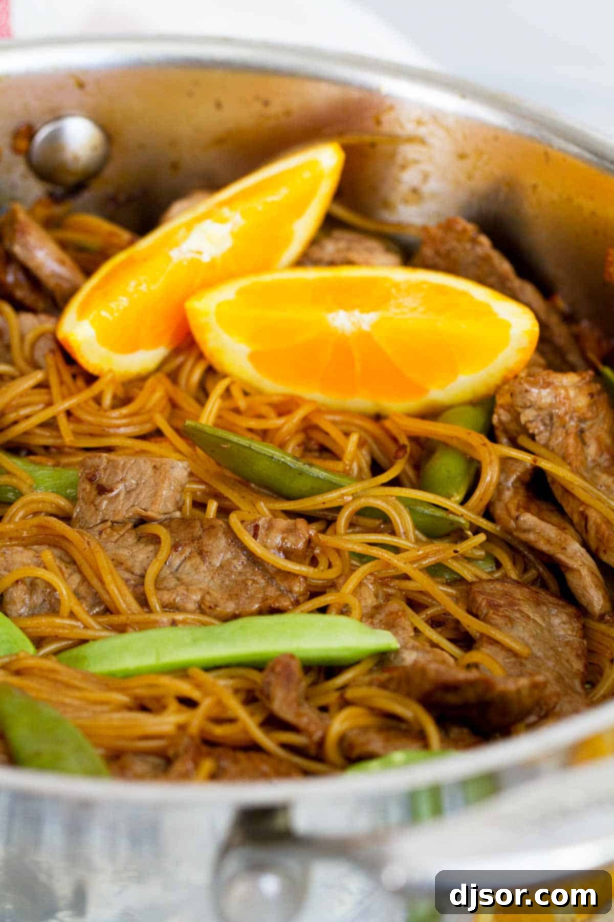A generous serving of Orange Teriyaki Beef with Noodles, beautifully presented in a bowl and garnished with fresh orange zest and green onions.
