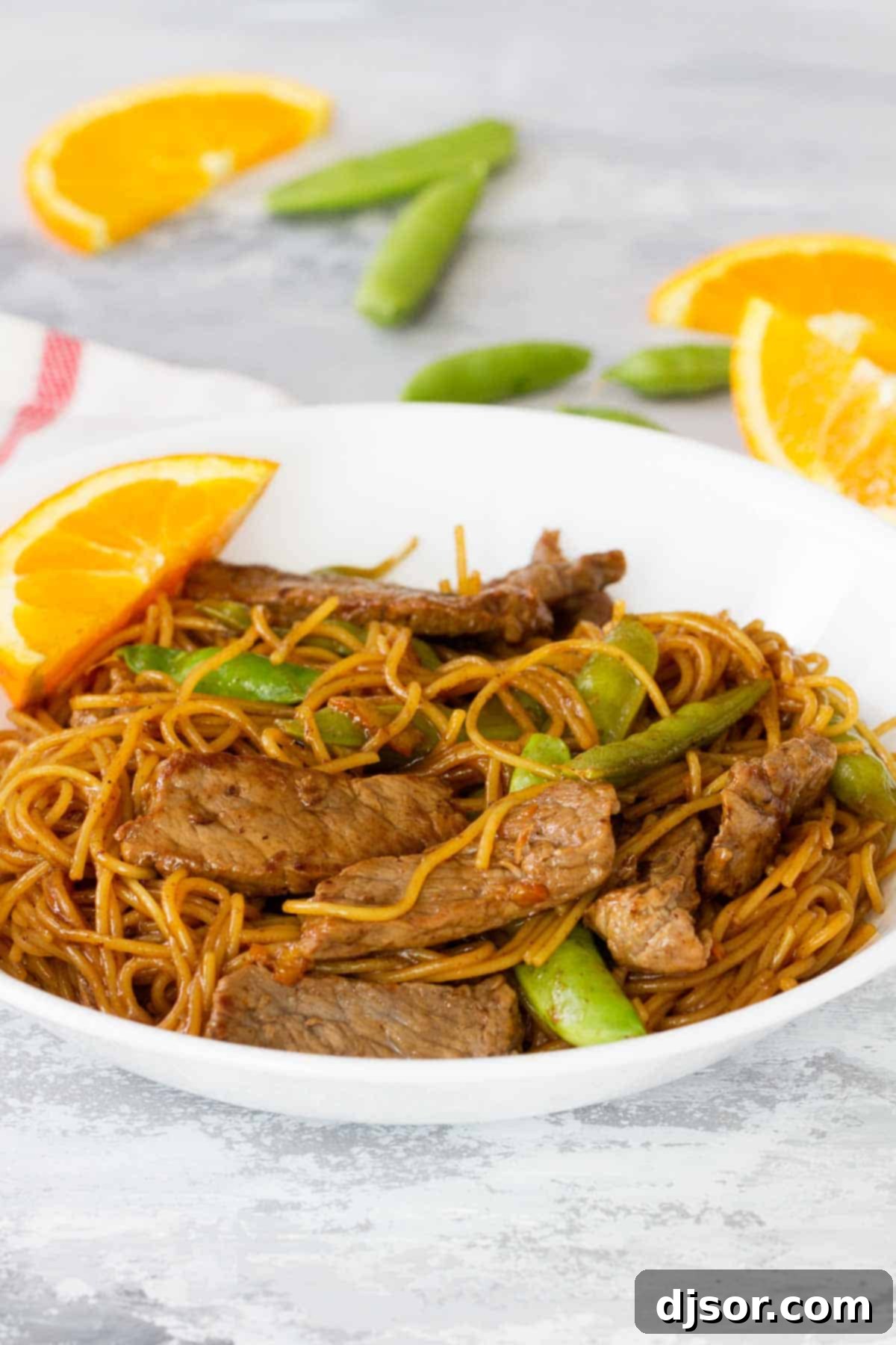 A close-up shot of Orange Teriyaki Beef with Noodles and sugar snap peas, artfully arranged in a bowl.