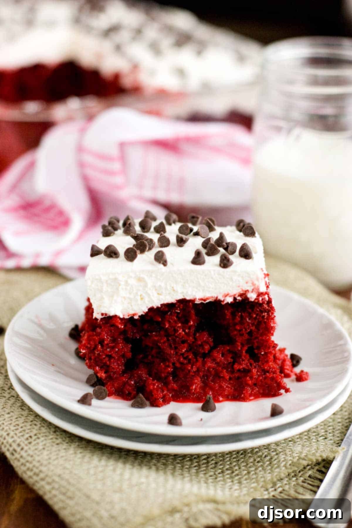 A beautiful slice of Red Velvet Tres Leches Cake, showcasing its moist texture and topped with mini chocolate chips, presented on a white plate.