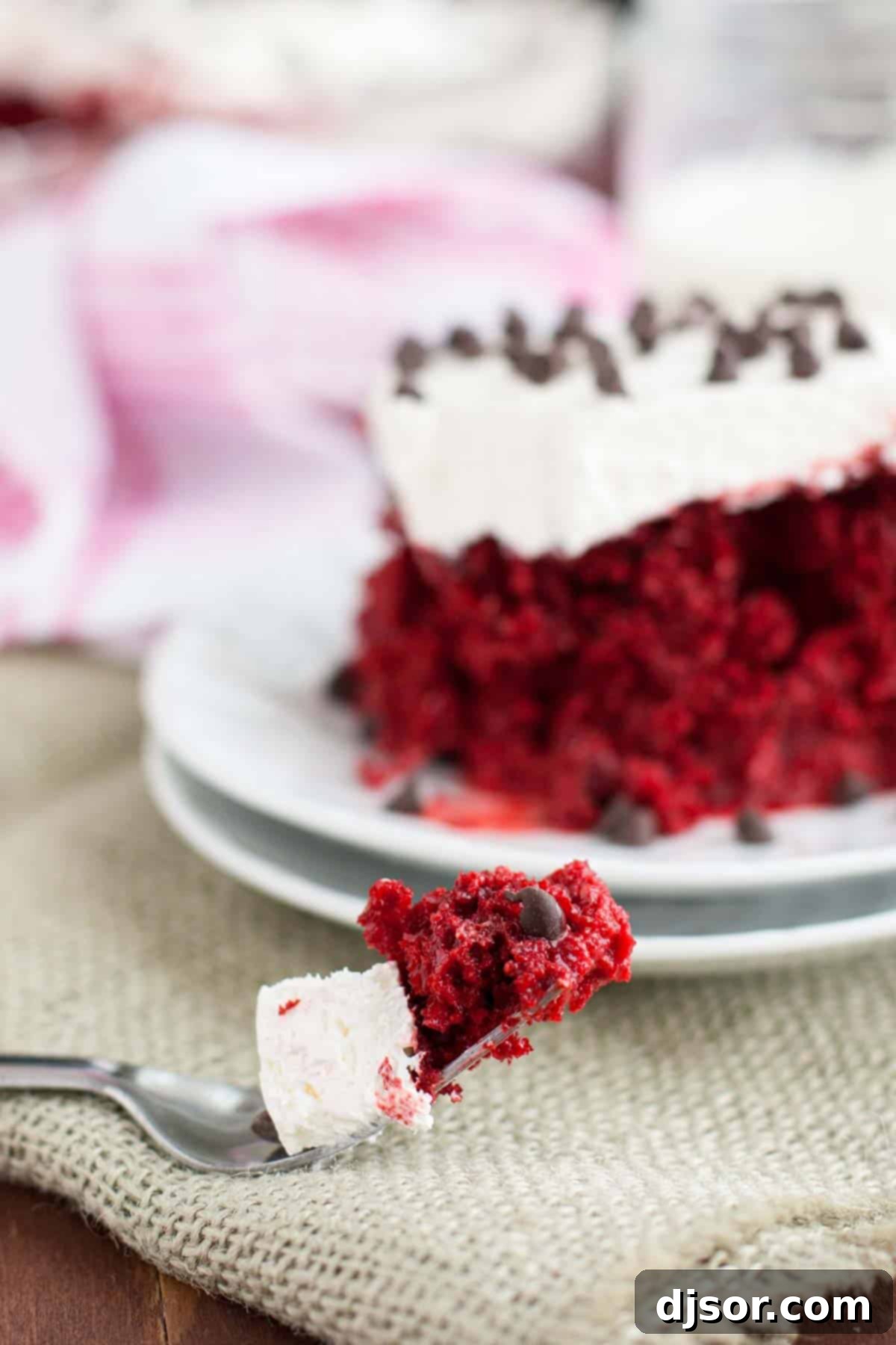 A fork taking a bite from a slice of Red Velvet Tres Leches Cake, showing the creamy whipped topping and moist cake layers.