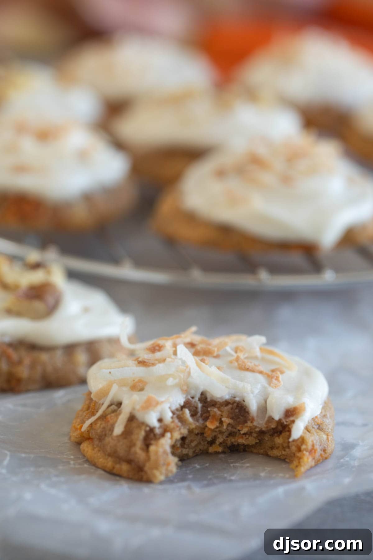 Carrot Cake Drops 9 Carrot Cake Cookies with cream cheese frosting with a bite taken from one cookie.
